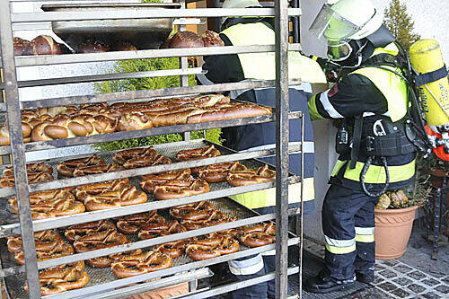 Brand in Kirchheimer Backstube: Feuerwehrleute schieben Wägen mit Laugengebäck aus dem Gebäude