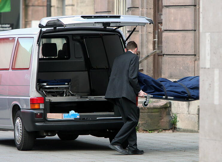 Ein Bestatter trägt die Bahre mit der Leiche des Obdachlosen zu einem Leichenwagen.