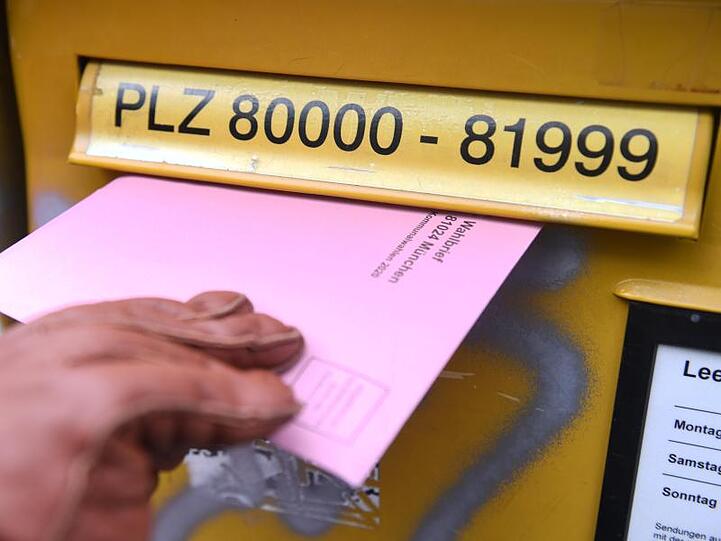 Eine Frau mit den Briefwahlunterlagen für die Kommunalwahl 2020 vor einem Briefkasten.