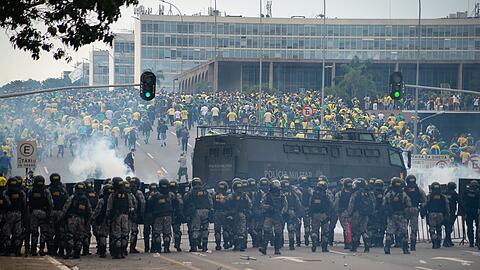 Anhänger des ehemaligen brasilianischen Präsidenten Bolsonaro (hinten) geraten in der Hauptstadt mit Ordnungskräften aneinander, die hinter Absperrungen eine Kette bilden und Tränengasgranaten auf die Demonstranten abfeuern. Auch ein gepanzerter Wasserwerfer ist im Einsatz. Anhänger des ehemaligen brasilianischen Präsidenten Bolsonaro haben den Kongress in der Hauptstadt Brasília gestürmt. +++ dpa-Bildfunk +++